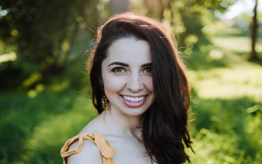 Portrait of founder Alexandra smiling in a forest landscape.